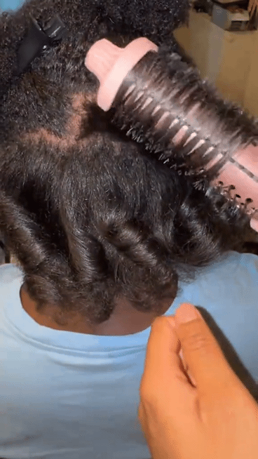 Une femme de dos avec les cheveux afro en train de se faire lisser et boucler les cheveux avec la brosse chauffante thermique