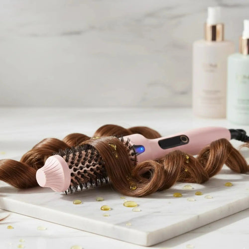 Brosse chauffante lissante placé sur un plateau de marbre avec une mèche enroulée autour de la brosse